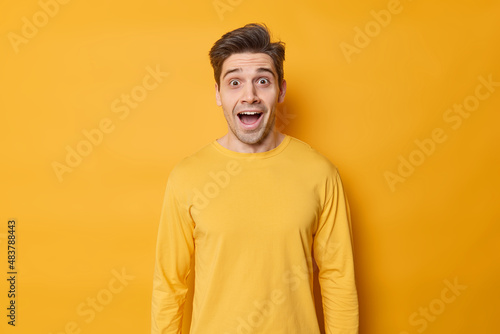 Overemotive surprised European man yells from pleasure and surprise keeps mouth opened dressed in casual jumper poses against yellow background astonished with great news retells it to friend © wayhome.studio 