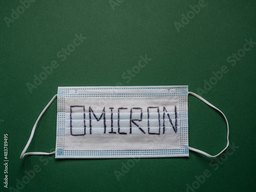 Face mask with word Omicron written on it and green background with copy space