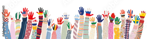 Arms raised up of multicultural children who have palms colored with the flags of various nations and countries. Group of multiethnic children and infants of different culture. Community