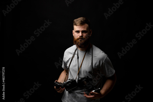 Professional handsome bearded male photographer with bunch of vintage photo cameras in photo studio, isolated on black background.