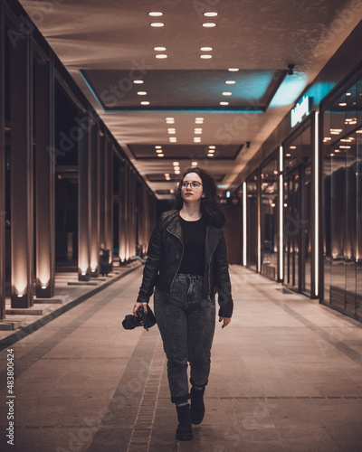 Portrait of a beautiful woman photographer dressed in black with a camera in her hand, walking through the city.