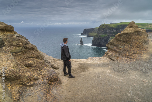 Man standing on the edge of iconic Cliffs of Moher and looking at sea stack underneath, popular tourist attraction, UNESCO, Wild Atlantic Way, Ireland photo
