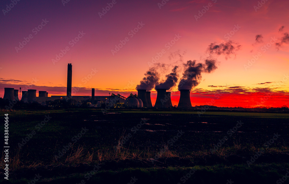Silhouette of a power station against a winter sunrise near Drax in North Yorkshire, UK with plumes of water vapour rising from the cooling towers.  Horizontal.  Copy space