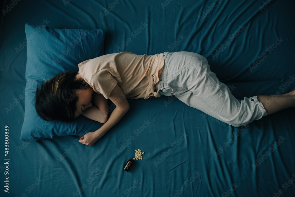 Top view of a young woman in bed with pills lying next to her. Concept of depression or mental health problems. Top view of a young woman in bed with pills lying next to her. Concept of depression or mental health problems.