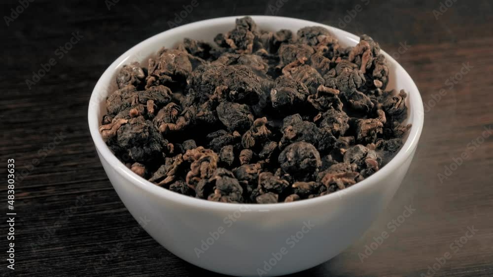 Green Chinese tea leaves in white cup on wood table. Oolong. Escaping Steam. Natural ingredients on the table. Healthy organic. Macro footage. Green Chinese tea leaves in white cup on wood table. Oolong. Escaping Steam. Natural ingredients on the table. Healthy organic. Macro footage.