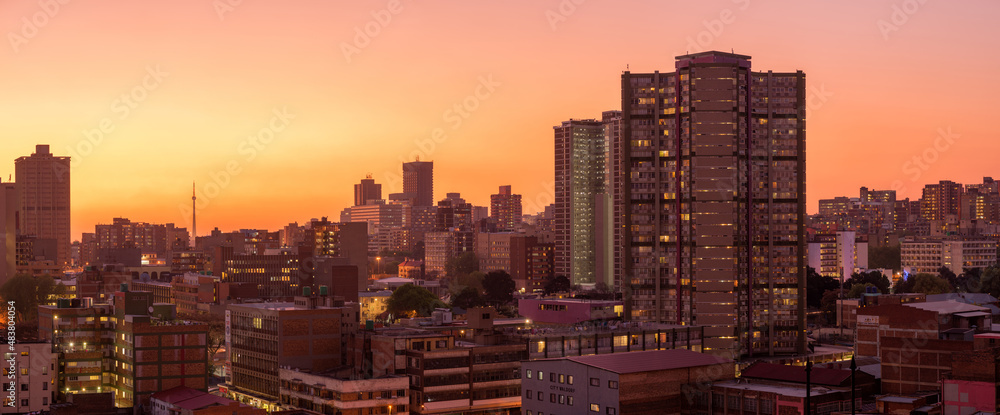 Naklejka premium A horizontal panoramic cityscape taken after sunset, against a pink and orange sky, of the central business district of the city of Johannesburg, South Africa