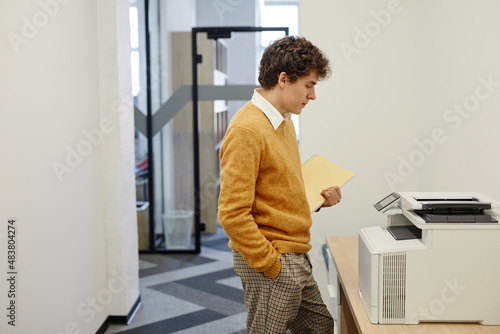 Side view portrait of young man using copying machine in office, copy space