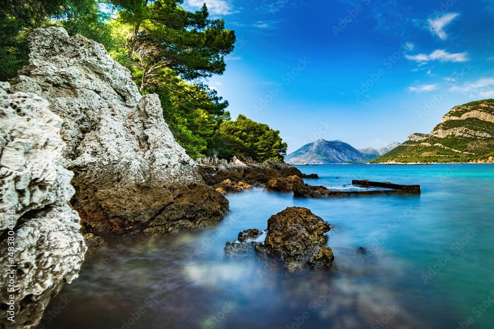 Fototapeta premium Wybrzeże i morze Chorwacji z kamienną plażą i niebieskim niebem z białymi chmurami