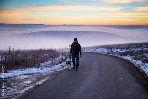 man with his dog in foggy winter landscape at sunset