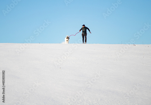 man and his happy white dog enjoying winter snow outdoors on sunny day