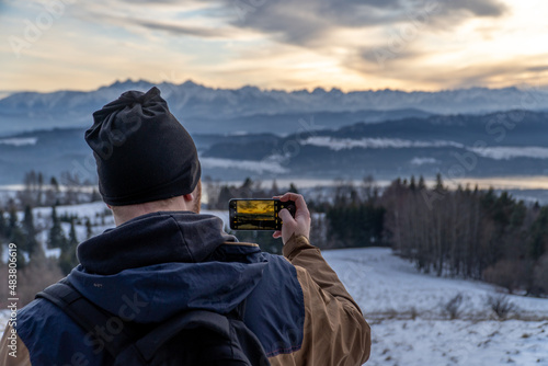 Mobile photography: man photographer taking picture of landscape when sunset at mountain peak. Travel and hobbies concept. Lake and mountains