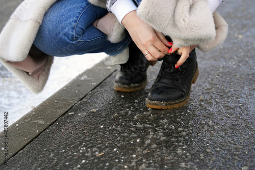 Women's hands with pink nails tie a shoelace on wet asphalt in winter
