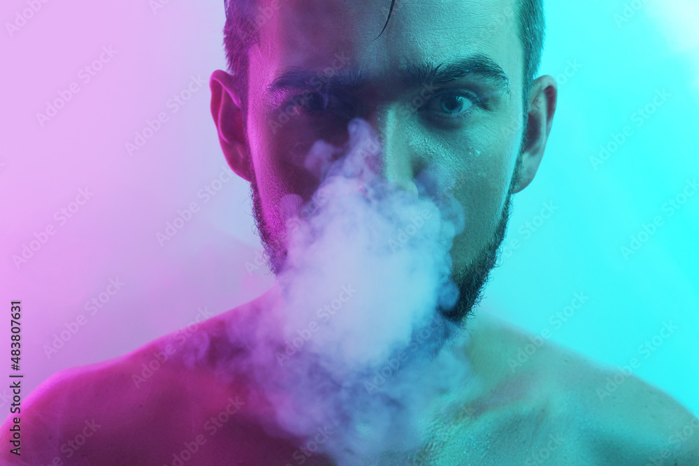Handsome young man with wet skin in ultraviolet light smoking vape