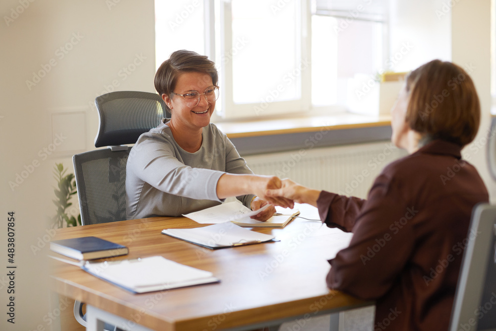 Portrait of female HR manager handing contract to young woman at job interview in office, copy space Portrait of female HR manager handing contract to young woman at job interview in office, copy space