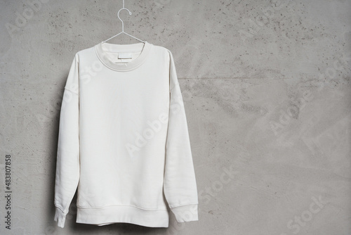 White sweatshirt hanging on the thin metallic hanger against a concrete wall