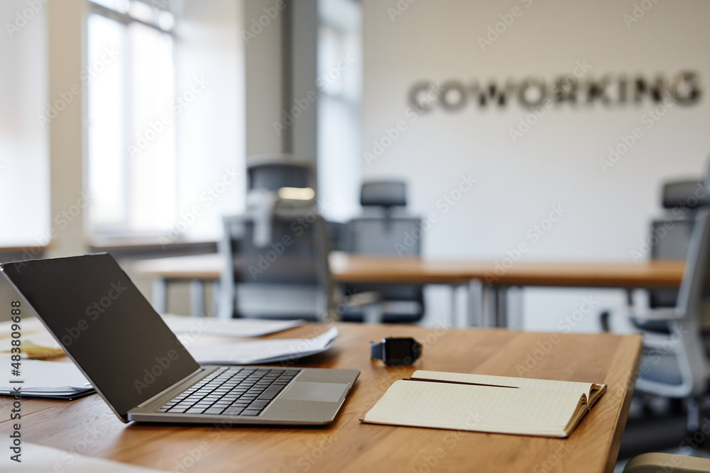 Side view close up of open laptop on desk in empty coworking space, copy space Side view close up of open laptop on desk in empty coworking space, copy space