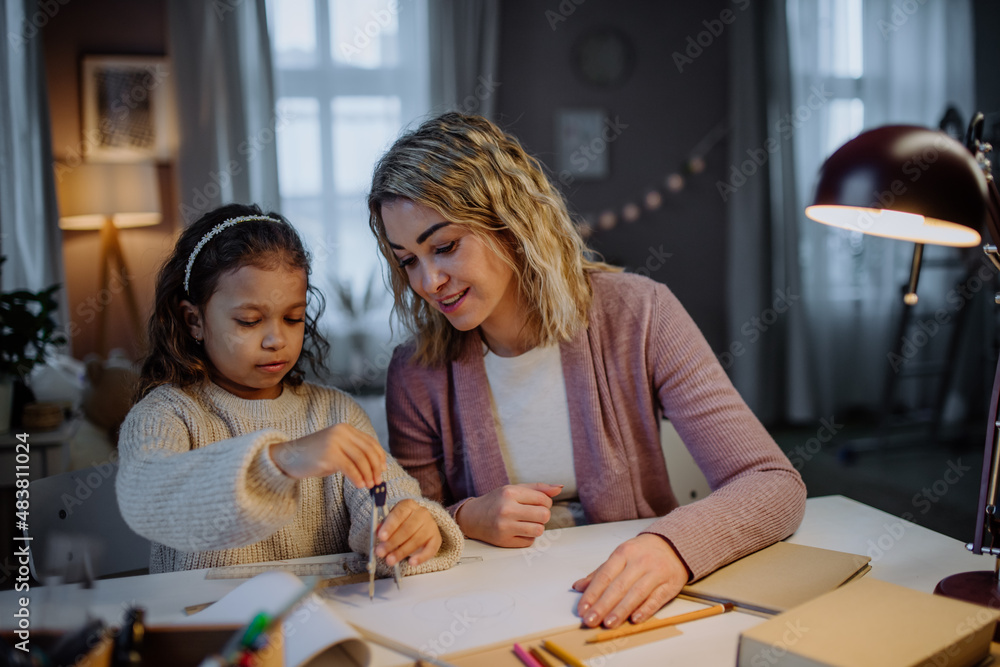 Mother helping her daughter with homework, drawing a circle with comasses in evening at home. Mother helping her daughter with homework, drawing a circle with comasses in evening at home.