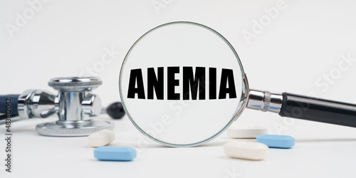 On a white surface lie pills, a stethoscope and a magnifying glass with the inscription - ANEMIA