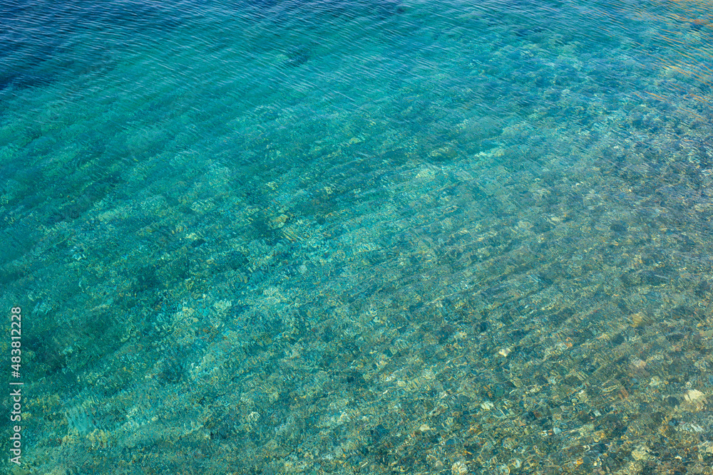 Texture of transparent turquoise blue rippling water of the sea with small stones under the surface