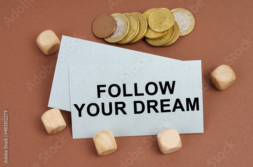 On a brown surface are coins, cubes and a business card with the inscription - FOLLOW YOUR DREAM