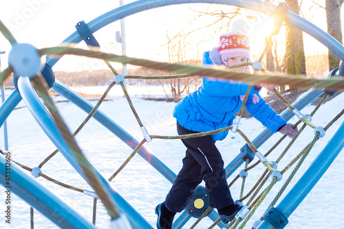 The child, a little Caucasian girl plays on the playground in the city park and is happy. Spring sun.