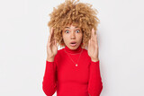 Omg how big it is. Amazed curly haired woman raises palms and shows huge gesture demonstrates size of something wears red turtleneck isolated over white background displays product shows items