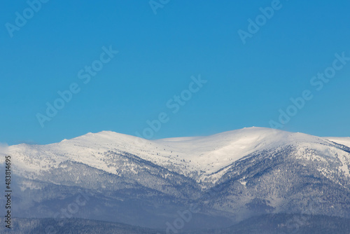 snow-capped mountain peaks with coniferous forests and clouds in the blue sky © Елена Челышева