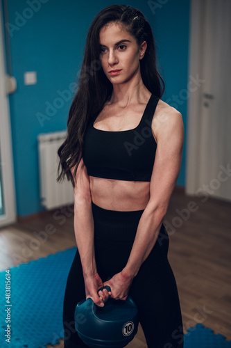 Portrait of a young woman holding a kettlebell while training in the gym