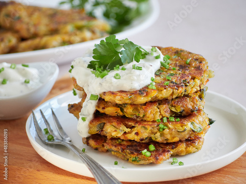 close up view of vegetarian pancakes stack, vegetable fritters, served with sour cream and fresh parsley.