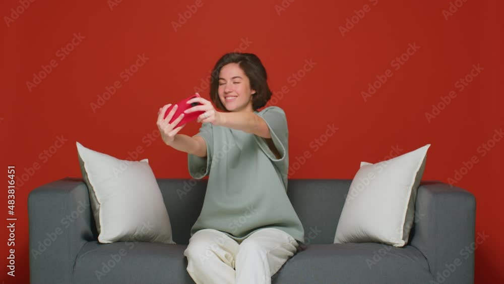 A cheerful cheerful girl at home plays mobile online games on a smartphone. Leisure time sitting on the couch. Weekend. A cheerful cheerful girl at home plays mobile online games on a smartphone. Leisure time sitting on the couch. Weekend.