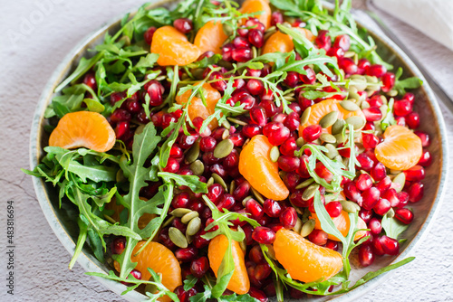 Fruit vitamin salad of pomegranate, tangerine, arugula and pumpkin seeds in a plate on the table. Organic vegetarian food. Close-up
