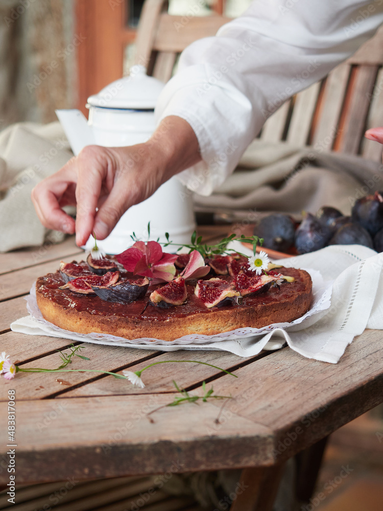 hand delicately decorating a fig tart with fresh edible flowers