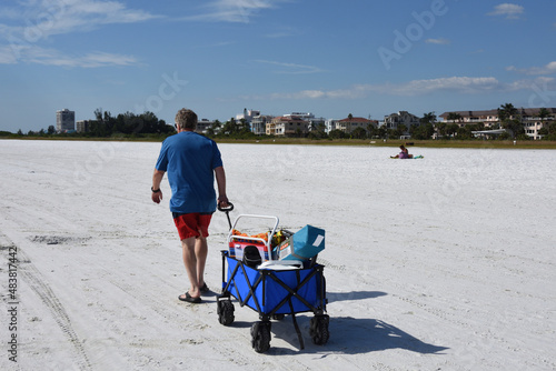 A rear view of Caucasian man pulling a wagon on the beach. Siesta Key Beach, Sarasota, Florida, USA.