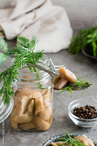 Pickled mushroom on a fork on a jar with boletus and dill and in a glass jar on the table. Vegetarian organic food. Vertical view. Close-up.