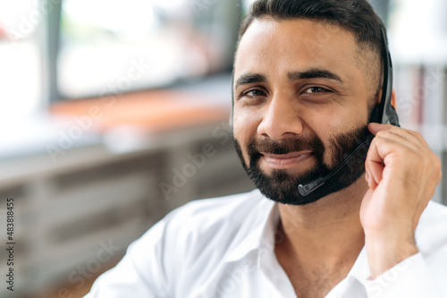 Close-up headshot of attractive, smart, successful Indian man, consultant or top manager, successful real estate agent, wearing headphones, formal wear, looking at camera, smiling pleasant
