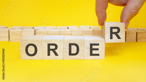 man making word ORDER with wooden cubes at yellow table, closeup. Space for text