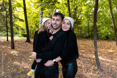 Dad, mom and daughter. The family hugs in the park. Summer park. Green trees. The concept of a young family. The decoration with stars is woven into the girl's hair. Happy family. © Sarbinaz Mustafina