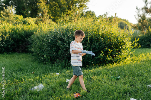 A seven-year-old boy at sunset is engaged in garbage collection in the park. Environmental care, recycling.