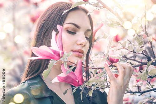 Beauty young woman enjoying nature in spring spring magnolia flowers. Beautiful brunette girl in Garden with blooming magnolia trees. Smiling girl with blossom flowers outdoors. Fashion model portrait
