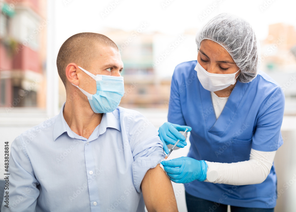 Professional female nurse injecting vaccine in shoulder of male patient during covid vaccination in clinic or hospital