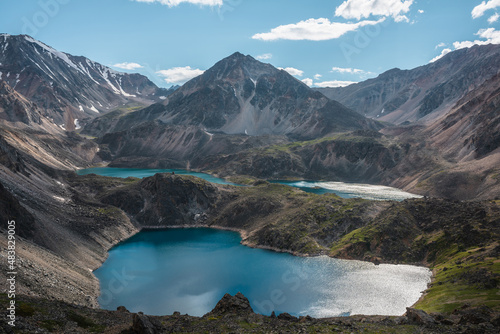 Scenic view to beautiful group of blue mountain lakes at various heights among black rocks in bright sun. Three blue lakes at different highs among sunlit black green rocky hills and large mountains.