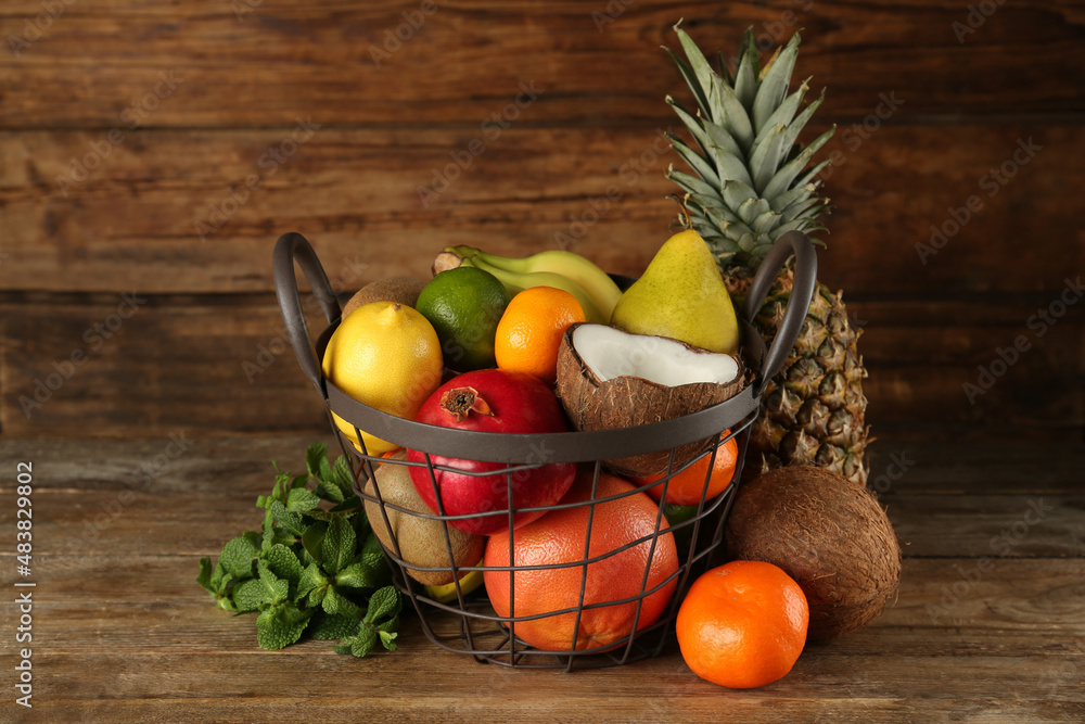 Metal basket and different ripe fruits on wooden table