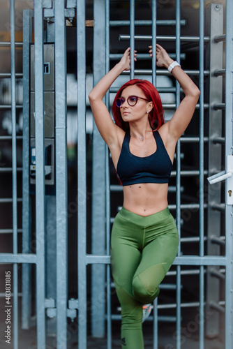 Fitness woman in sportswear doing stretching exercise on the city street, concrete background. © aboutmomentsimages