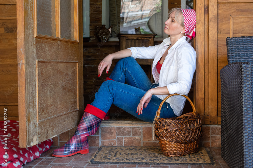Φωτογραφία Blond middle aged woman is resting in the doorway of her house