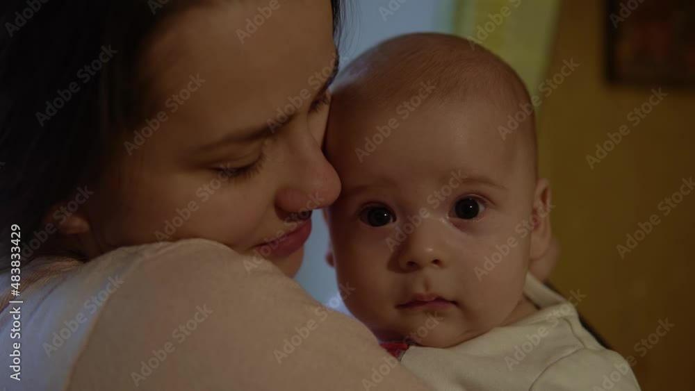 Authentic shot young neo happy mother is keeping in arms and caressing smiling newborn baby Child kid in Evening night at home. Concept maternity, motherhood,parenthood, childhood, life, authenticity