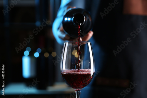 Obraz na plátně Bartender pouring red wine from bottle into glass indoors, closeup