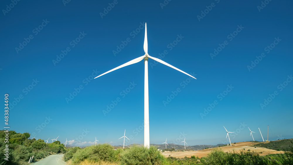 One huge wind generator in front of Oreites wind farm in Cyprus against clear blue sky. Panorama landscape with wide angle lens dramatic distortion One huge wind generator in front of Oreites wind farm in Cyprus against clear blue sky. Panorama landscape with wide angle lens dramatic distortion