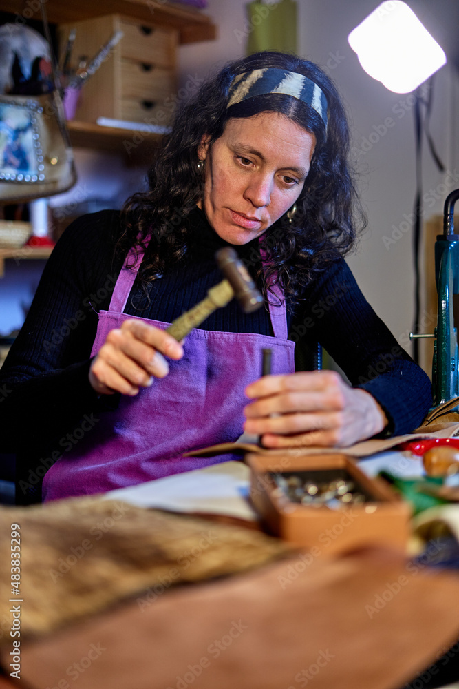 Fototapeta premium Craftswoman hammering leather at the work table in her studio