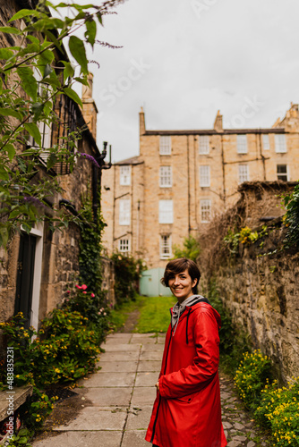 Young female posing with a red raincoat in the middle of a close during a rainy summer day in Edinburgh.