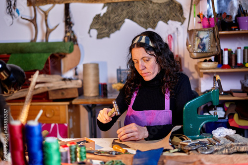 Craftswoman hammering leather at the work table in her studio